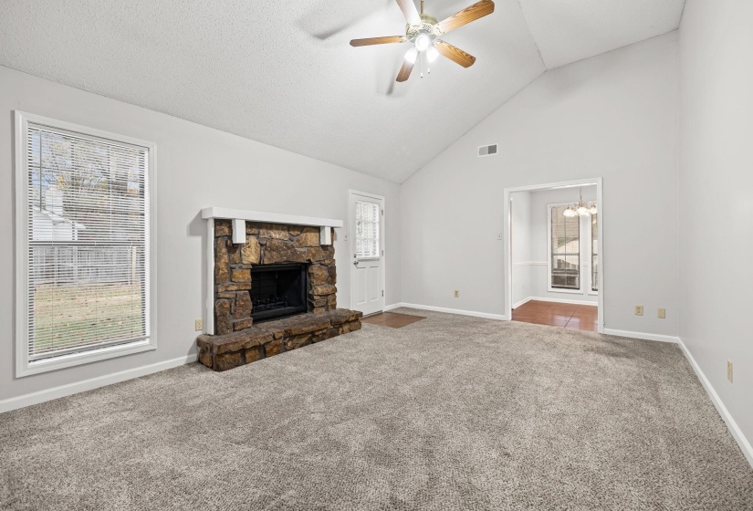 Unfurnished living room with carpet, a stone fireplace, high vaulted ceiling, ceiling fan, and a chandelier