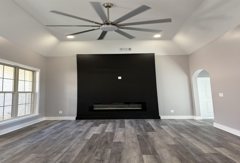 Unfurnished living room featuring lofted ceiling, light wood-type flooring, a ceiling fan, a glass covered fireplace, and arched walkways