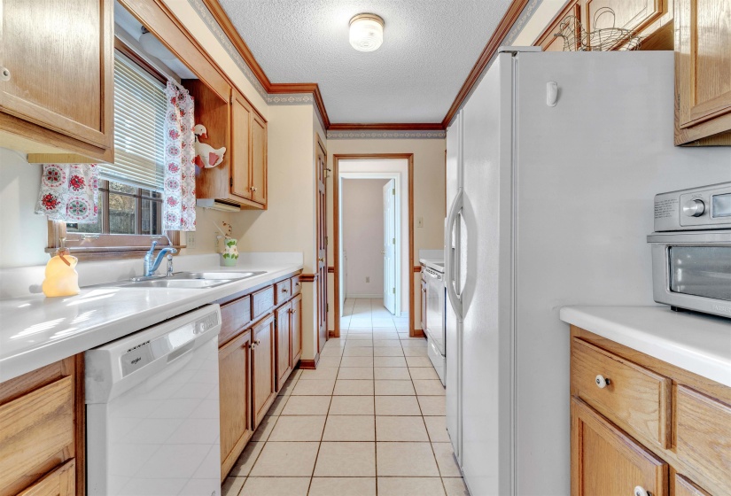 Kitchen with white appliances, ornamental molding, a textured ceiling, light countertops, and light tile patterned flooring