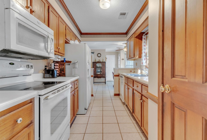 Kitchen with white appliances, crown molding, light tile patterned floors, light countertops, and a textured ceiling