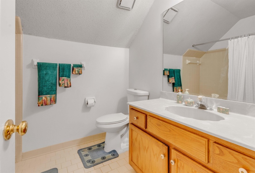 Bathroom featuring light tile patterned floors, vanity, a shower with shower curtain, vaulted ceiling, and a textured ceiling