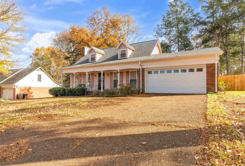 View of front facade featuring covered porch, dirt driveway, brick siding, and a chimney