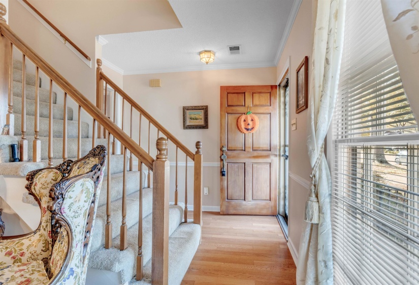 Foyer entrance with ornamental molding, light wood-style flooring, and stairway