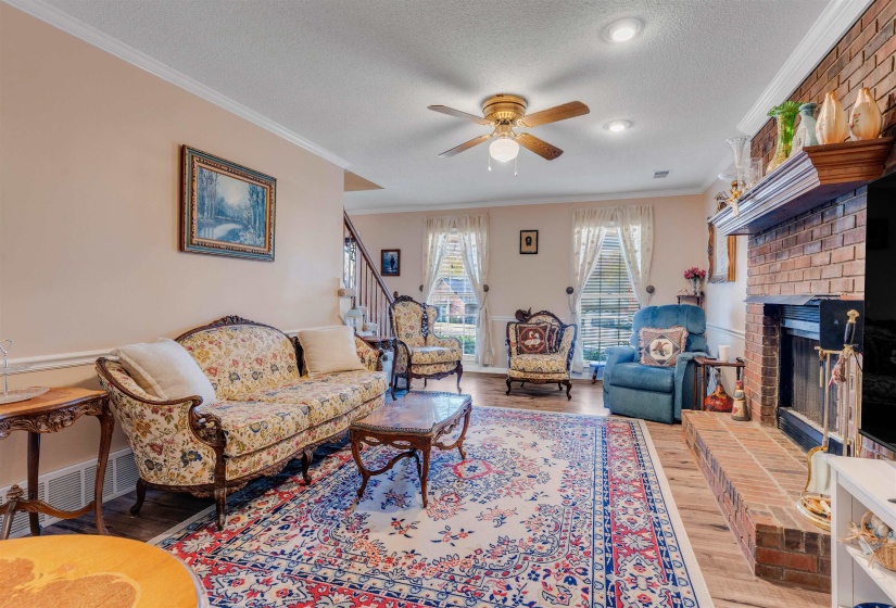 Living room with ornamental molding, wood finished floors, a textured ceiling, ceiling fan, and stairway