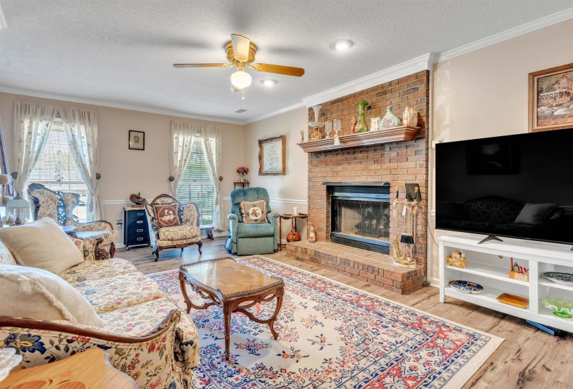 Living area with a textured ceiling, ornamental molding, a brick fireplace, ceiling fan, and light wood finished floors