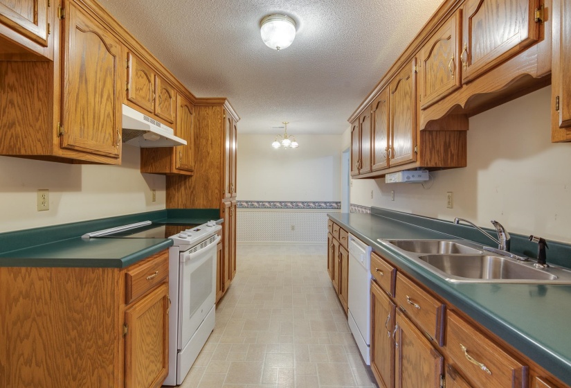 Kitchen with white appliances, brown cabinetry, a textured ceiling, under cabinet range hood, and a chandelier
