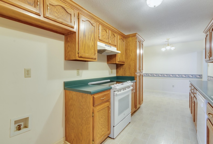 Kitchen featuring white appliances, under cabinet range hood, a textured ceiling, pendant lighting, and brown cabinets