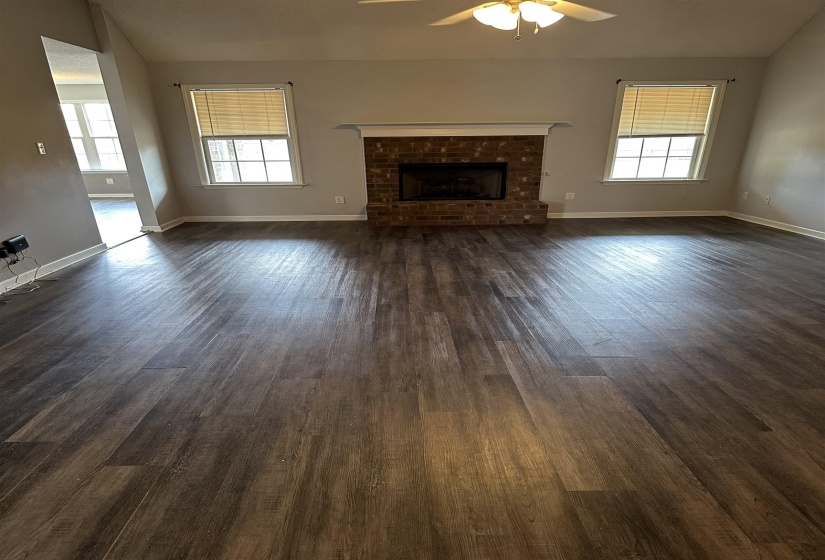 Unfurnished living room featuring vaulted ceiling, dark wood finished floors, a brick fireplace, and ceiling fan