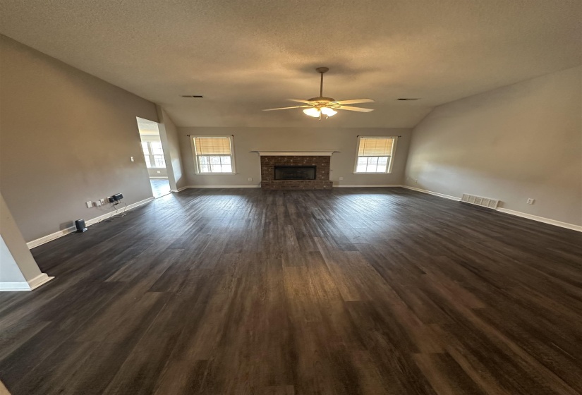 Unfurnished living room with lofted ceiling, dark wood finished floors, a ceiling fan, a fireplace, and a textured ceiling