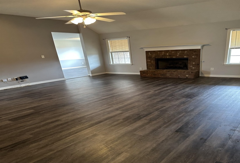 Unfurnished living room with lofted ceiling, dark wood-style flooring, a fireplace, ceiling fan, and healthy amount of natural light