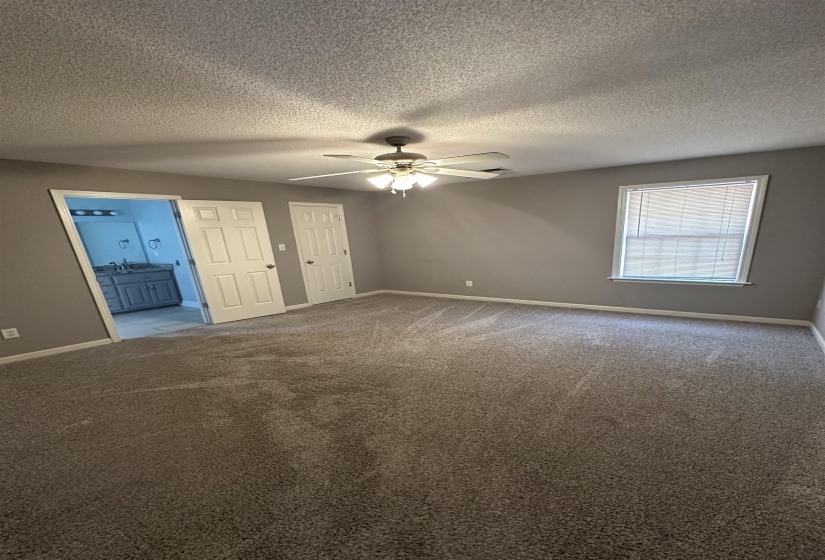 Unfurnished bedroom with carpet flooring, ensuite bath, ceiling fan, and a textured ceiling