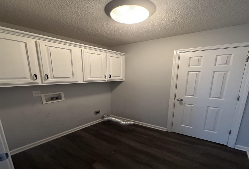 Laundry room featuring a textured ceiling, dark wood-style flooring, hookup for a washing machine, hookup for an electric dryer, and cabinet space