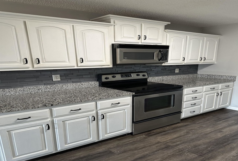 Kitchen featuring appliances with stainless steel finishes, white cabinetry, dark wood-style flooring, light stone countertops, and tasteful backsplash