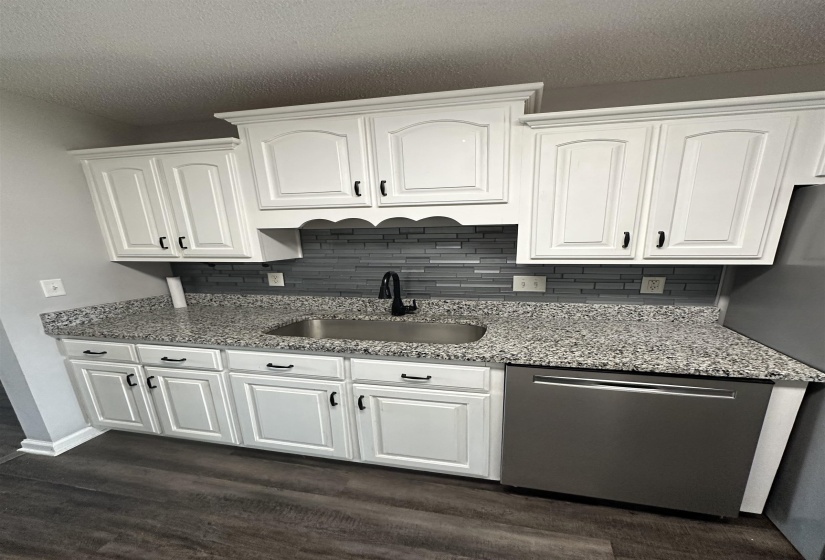 Kitchen with light stone countertops, white cabinetry, dark wood finished floors, and a textured ceiling
