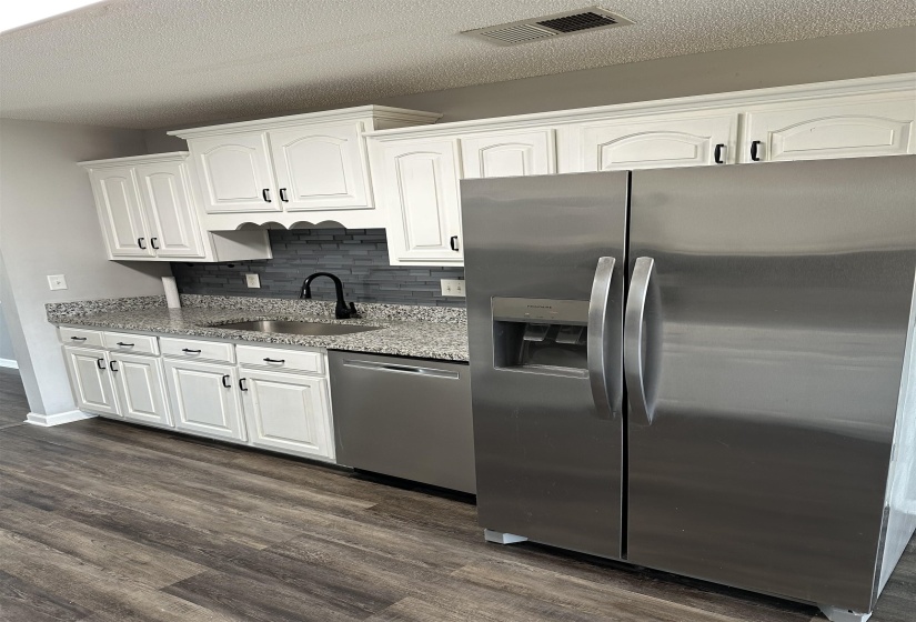 Kitchen with appliances with stainless steel finishes, light stone counters, white cabinetry, dark wood finished floors, and a textured ceiling