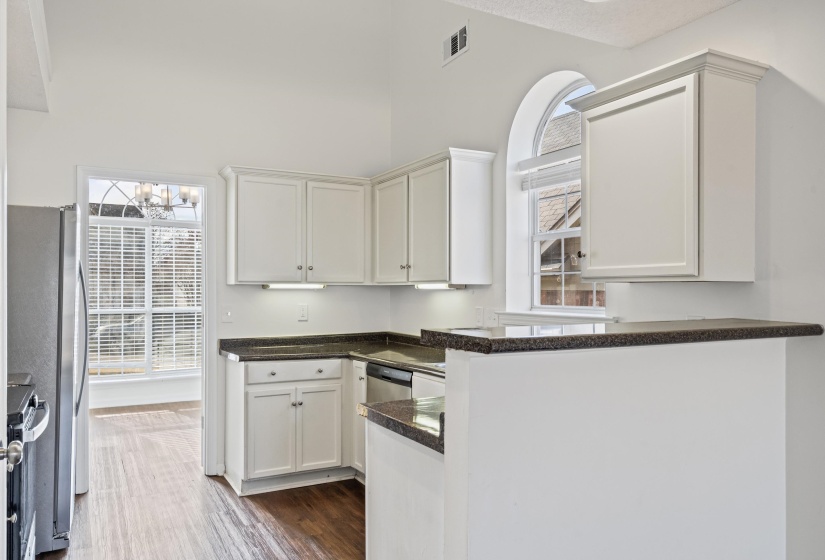 Kitchen with dark wood-style flooring, white cabinetry, stainless steel appliances, dark stone countertops, and a high ceiling