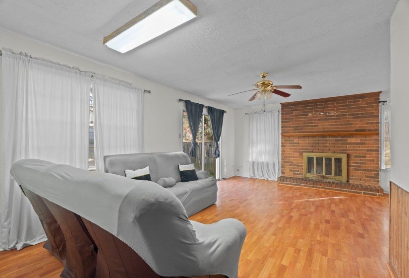 Living area with a textured ceiling, a brick fireplace, light wood finished floors, and a ceiling fan
