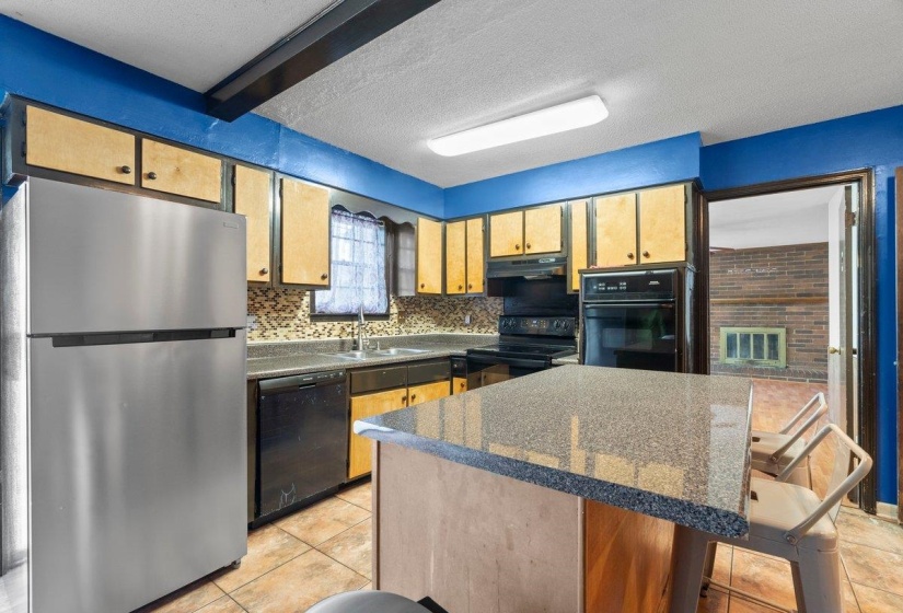 Kitchen featuring black appliances, a breakfast bar, decorative backsplash, a center island, and a textured ceiling