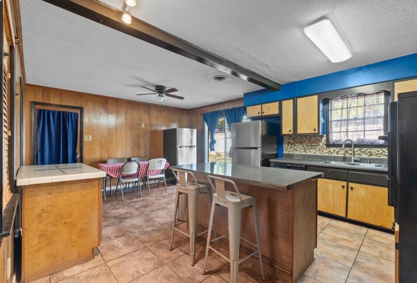 Kitchen with beam ceiling, a kitchen island, freestanding refrigerator, ceiling fan, and a textured ceiling