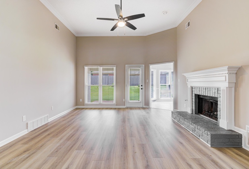 Unfurnished living room featuring ceiling fan, ornamental molding, wood finished floors, a brick fireplace, and baseboards