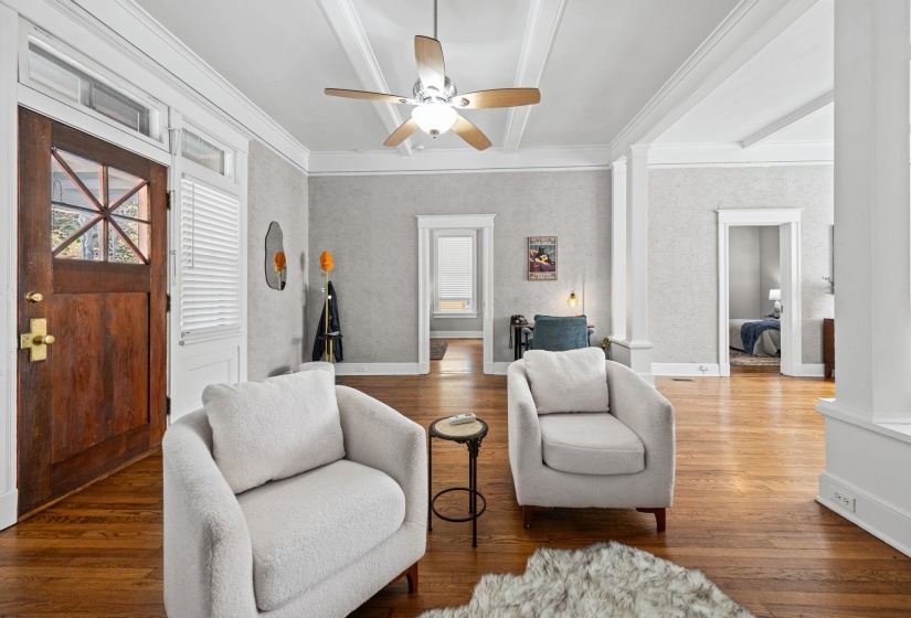 Living area featuring wood finished floors, ceiling fan, ornamental molding, beam ceiling, and decorative columns