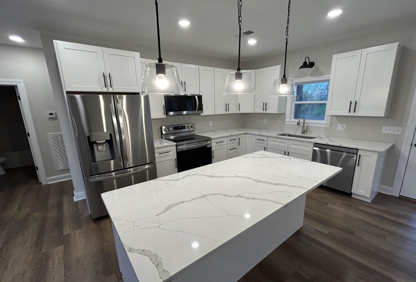 Kitchen with pendant lighting, stainless steel appliances, quartz countertops, and white shaker cabinetry.