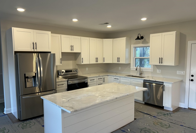 Kitchen featuring LG appliances with stainless steel finishes, white shaker cabinets, quartz countertops, and island.
