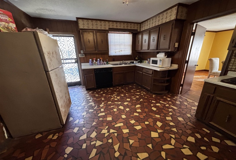 Kitchen with dark brown cabinetry, light countertops, white appliances, a textured ceiling, and wood walls
