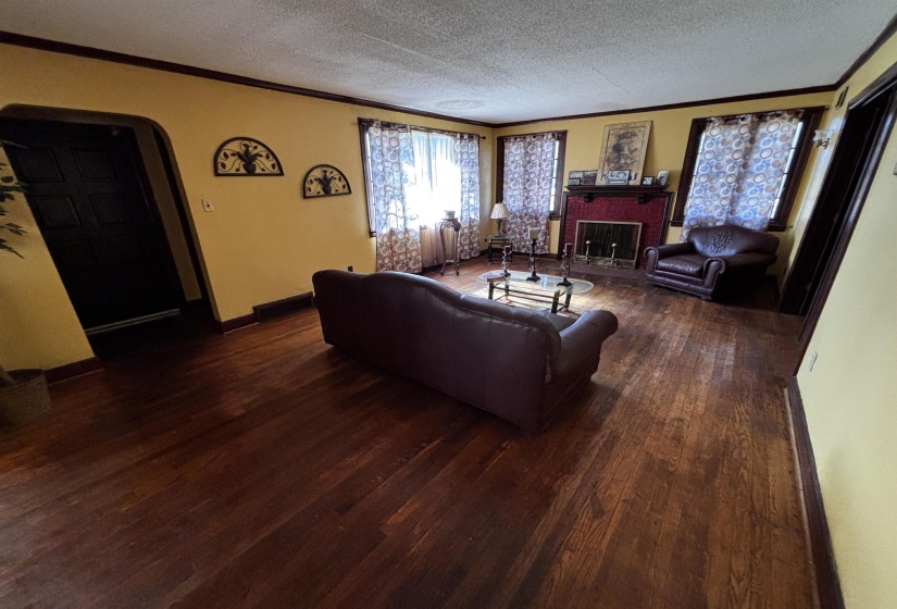 Living room with crown molding, arched walkways, a brick fireplace, a textured ceiling, and dark wood-style flooring