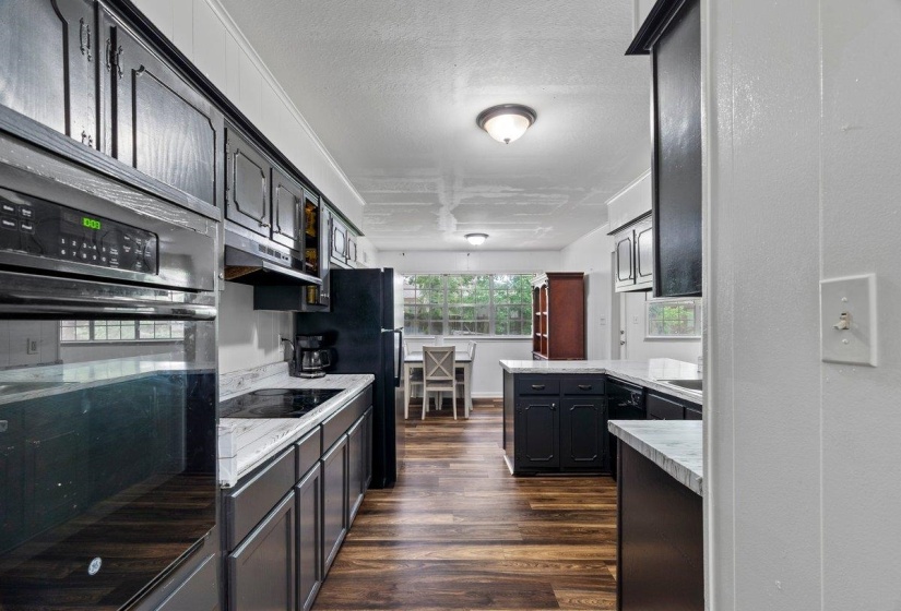 Kitchen featuring black appliances, dark wood finished floors, a textured ceiling, dark cabinetry, and under cabinet range hood
