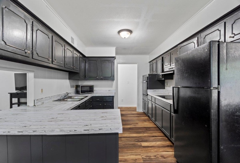Kitchen with black appliances, light countertops, dark wood-type flooring, a peninsula, and crown molding