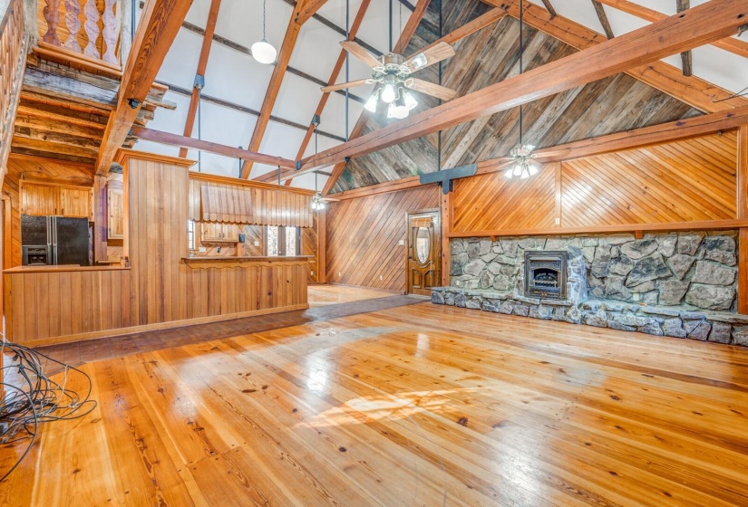 Unfurnished living room with light wood-type flooring, high vaulted ceiling, wooden walls, a ceiling fan, and beam ceiling