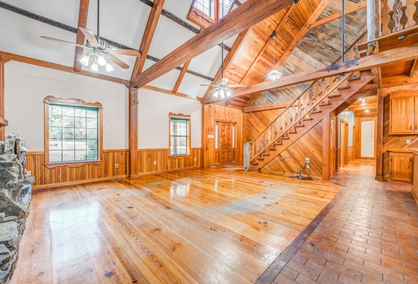 Unfurnished living room with high vaulted ceiling, wooden walls, stairway, light wood-style flooring, and beamed ceiling