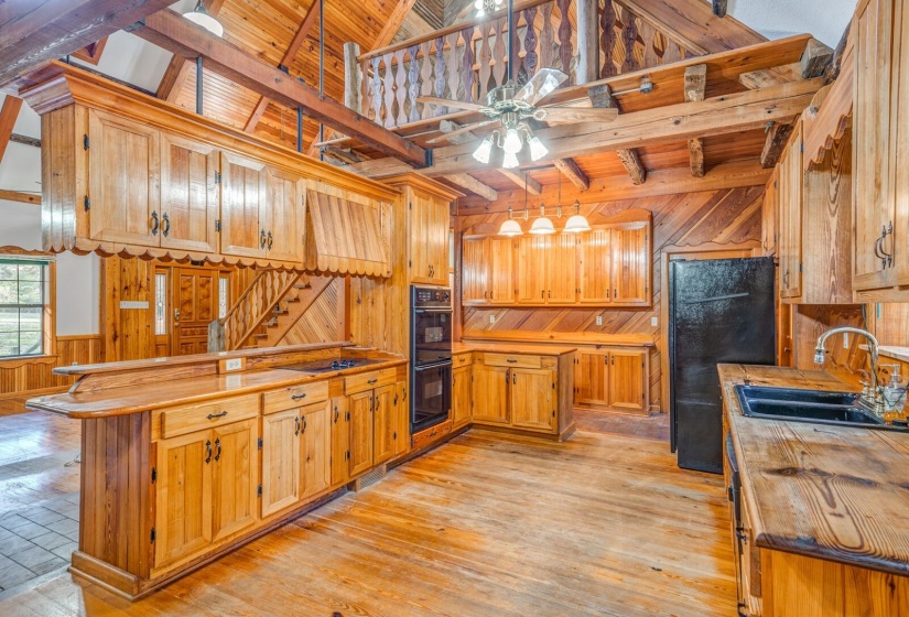 Kitchen with wooden walls, wood counters, brown cabinetry, wainscoting, and a peninsula