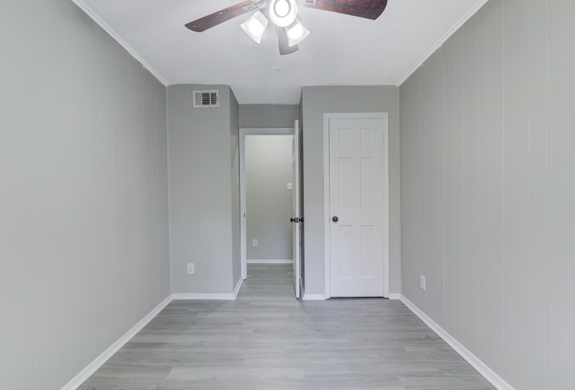 Unfurnished bedroom featuring light wood-style flooring, crown molding, ceiling fan, and wood walls