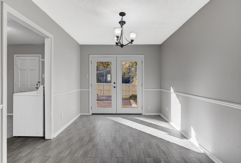 Unfurnished dining area featuring a textured ceiling, a chandelier, light wood finished floors, french doors, and washer / clothes dryer