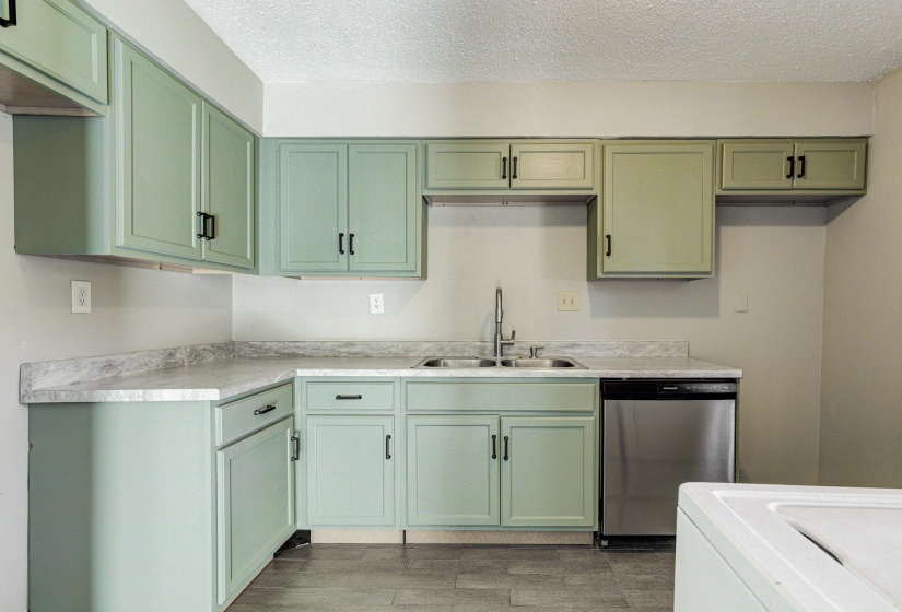 Kitchen with green cabinets, stainless steel dishwasher, a textured ceiling, light countertops, and washer / dryer