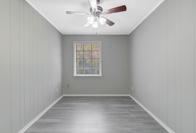 Unfurnished room featuring crown molding, light wood-style floors, a ceiling fan, a textured ceiling, and wooden walls