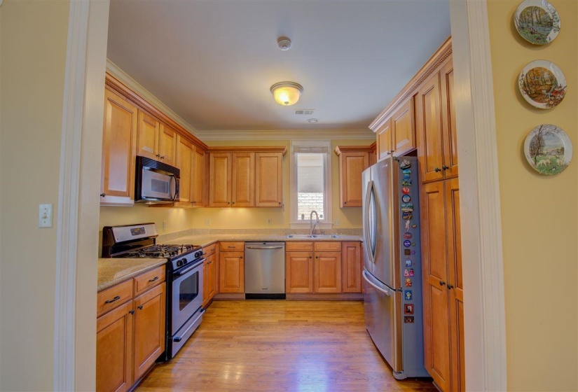Kitchen featuring stainless steel appliances, light wood-type flooring, ornamental molding, and light stone counters
