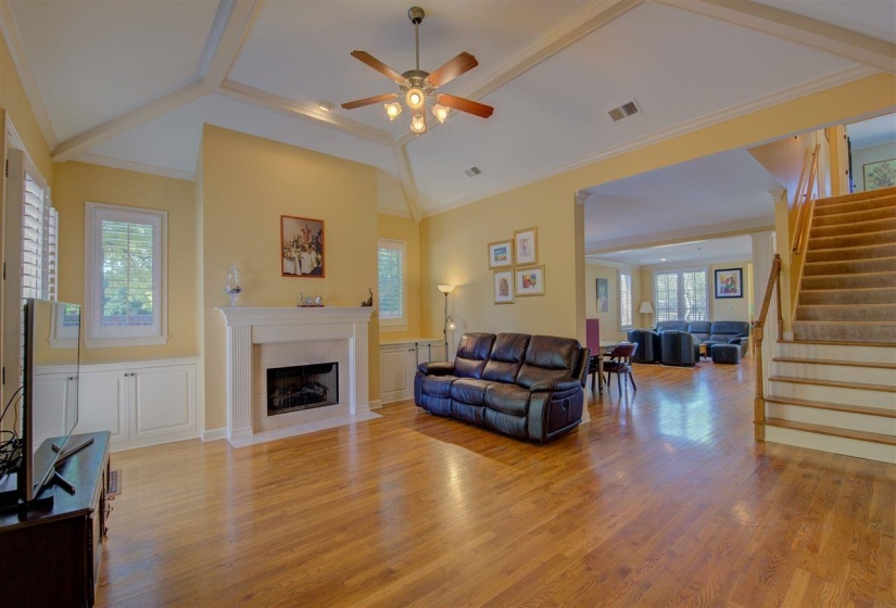 Living area featuring stairway, a fireplace, light wood-type flooring, a ceiling fan, and ornamental molding