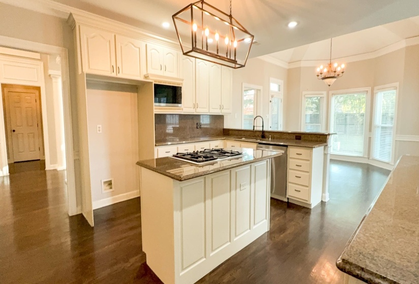 Kitchen with decorative backsplash, hanging light fixtures, dark stone countertops, a peninsula, and dark wood finished floors