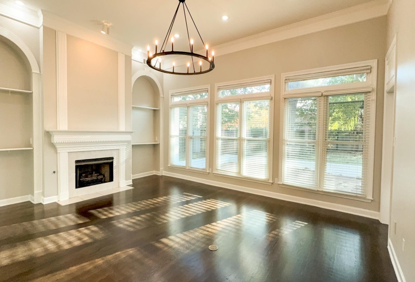 Unfurnished living room featuring built in features, ornamental molding, a fireplace with flush hearth, a chandelier, and dark wood-style floors