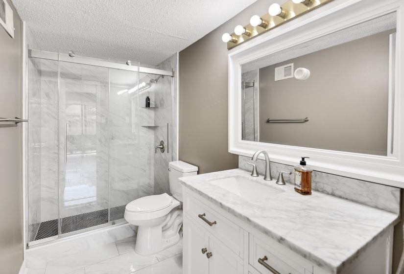 Bathroom with a textured ceiling, vanity, light marble finish flooring, and a marble finish shower