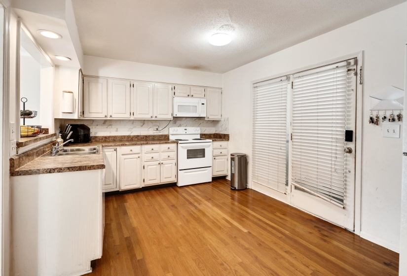 Kitchen with tasteful backsplash, dark countertops, white cabinets, light wood-type flooring, and white appliances