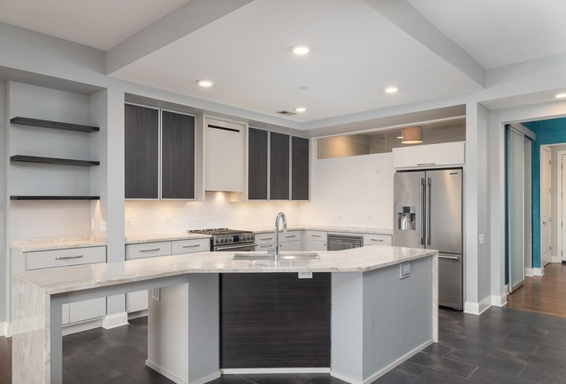 Kitchen featuring light stone counters, backsplash, premium appliances, open shelves, and an island with sink