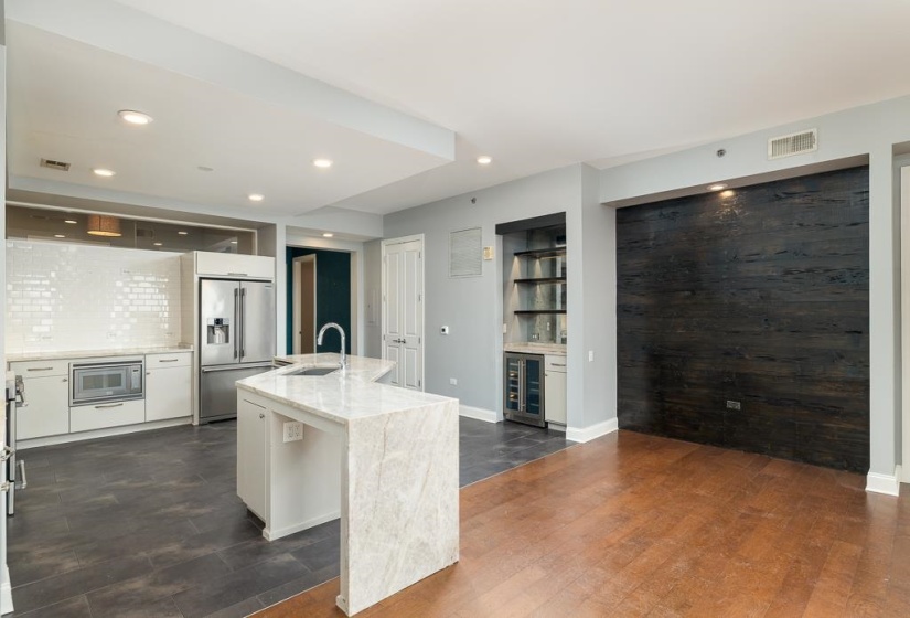 Kitchen featuring a center island with sink, light stone countertops, white cabinetry, beverage cooler, and high quality fridge