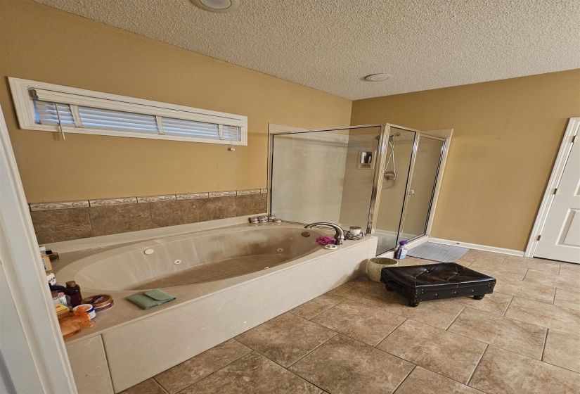 Bathroom featuring a stall shower, a whirlpool tub, a textured ceiling, double sinks, with walk in closet