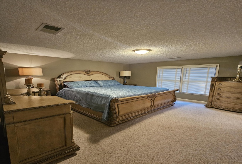 Bedroom with light colored carpet and a textured ceiling, walk in closet