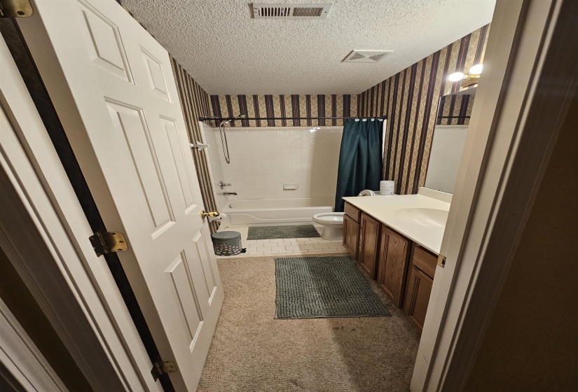Bathroom with vanity, shower / tub combo with curtain, a textured ceiling, wallpapered walls, and light carpet