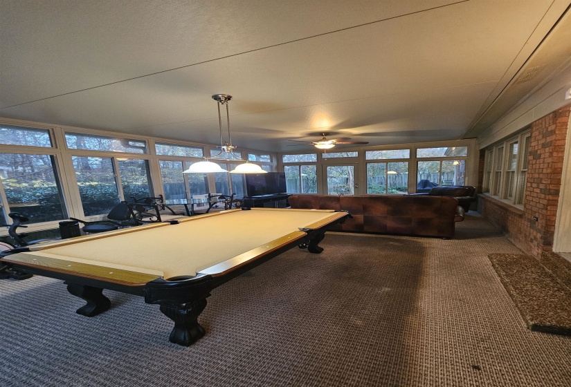 Recreation room featuring  carpet, a ceiling fan, and brick wall